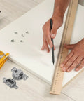 Person measuring and marking wood panel with ruler near Two Pack Inward Opening Folding Cabinet Hinges with Soft Close, screws, and drill.