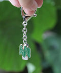 Front close-up of a silver keychain with an enamel plant charm—green leaves in a white pot, hanging from a chain