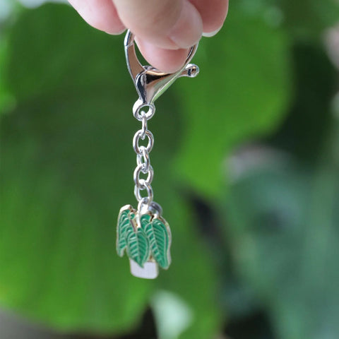 Front close-up of a silver keychain with an enamel plant charm—green leaves in a white pot, hanging from a chain