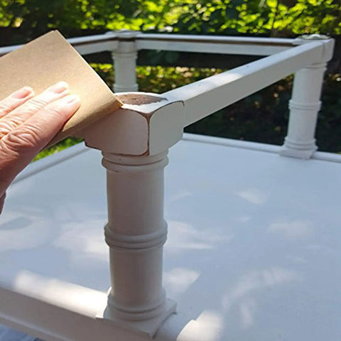 Hand using sandpaper from All In One Sandpaper Kit With 36 Wet Or Dry Grit Sheets From 120 To 3000 on wooden furniture corner.