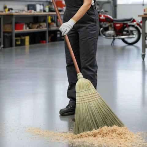 42 Inch Natural Fiber Wire Banded Warehouse Broom With Real Wood Handle For Sweeping Concrete Driveways Garages And Kitchens Built Tough To Handle The Daily Grind being used to sweep wooden debris on a concrete floor.