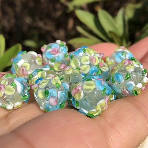 Score These Hella Rad Lampwork Glass Round Spacer Beads With Big Center Holes Perfect For DIY Jewelry Making Kicking Up Your Bracelet And Necklace Crafting Vibes Today, assorted blue and green floral beads in hand.