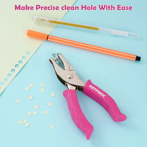 One Hole Punch With Soft Grip Handle For Paper One Quarter Inch Hole Punch Pink With Mess Tray Six Sheet Capacity Ideal For Crafts And Scrapbooks Great For DIY Projects on a blue background with pens and punched paper circles.