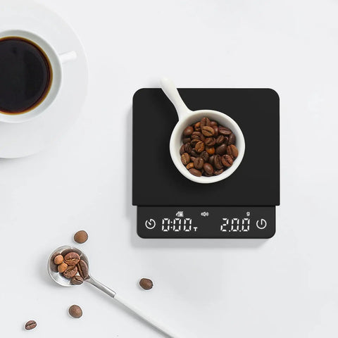 Black palmsized coffee scale with timer, measuring coffee beans near a cup, rechargeable USB C, 2Kg capacity, 0.1G precision.