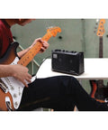 Musician playing guitar next to battery powered stereo amplifier for guitars and keyboards, totally portable mini PA with effects.