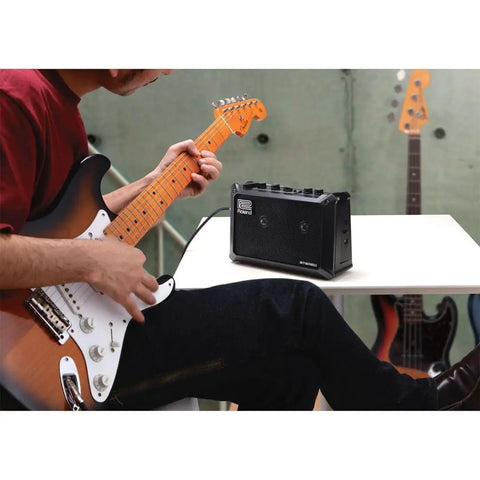 Musician playing guitar next to battery powered stereo amplifier for guitars and keyboards, totally portable mini PA with effects.