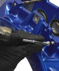 Using a Slick Brake Caliper Pad Pin Punch for stuck bolts on a blue brake caliper during maintenance.