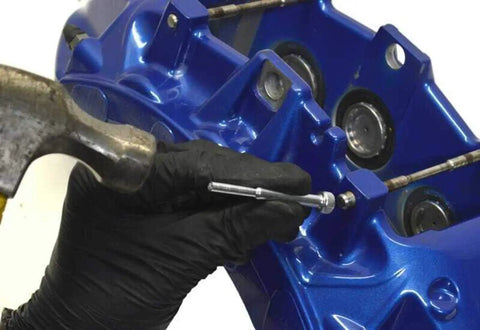 Using a Slick Brake Caliper Pad Pin Punch for stuck bolts on a blue brake caliper during maintenance.