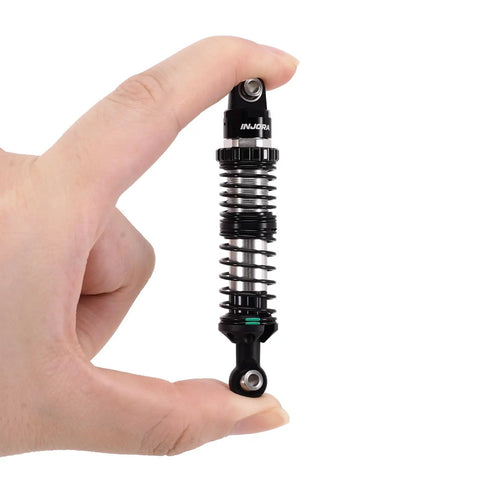 Dual Rate 100mm RC Crawler Shocks With Aluminum Bodies And Nylon Rod Ends For TRX4 SCX10 One Tenth Scale Heavy Duty Upgrade Includes 0.9mm And 1.0mm Spring Rates Eye To Eye 80 To 120mm Oil Not Included held between fingers