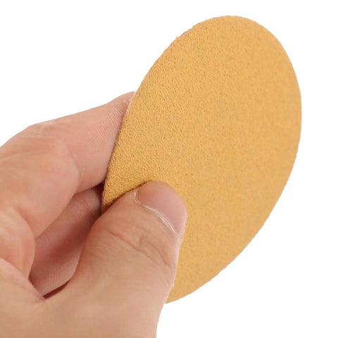 Hand holding a beige self-adhesive sanding disc from the 40 Pc Sanding Disc Grit Set for rust removal and refinishing.