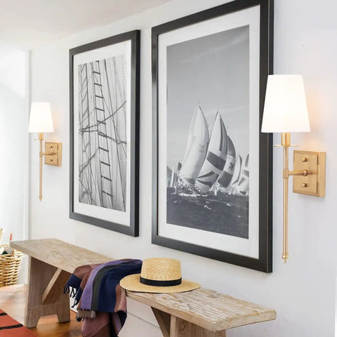 Sleek Modern Wall Sconces in Antique Brass Brush Finish With White Fabric Shade beside framed nautical art in hallway.