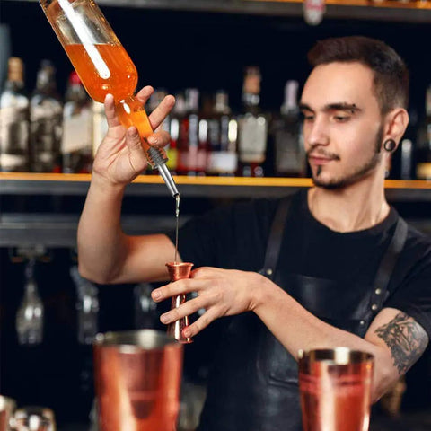 Set Of 2 Stainless Steel Pourers For Liquor Olive Oil And Vinegar Bottles With Tapered Stopper Spouts No Spill Control Sealed Dust Caps Fits About Three Quarters Inch Bottle Openings Durable And Easy To Clean Built Like A Tank. bartender pouring liquor with stainless steel pourer into a jigger