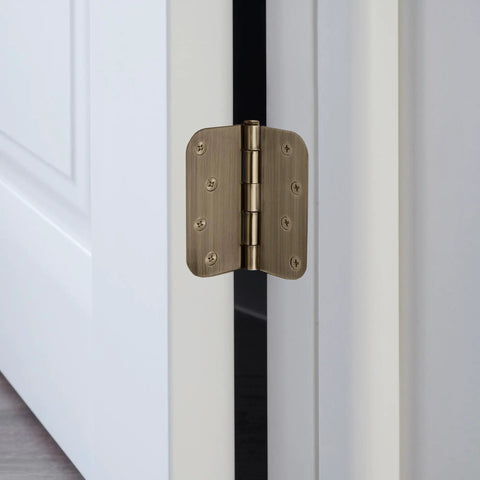 Built Thick Steel Interior Door Hinges Four Inch Antique Brass Finish Three Pack With Removable Pin For Smooth Daily Swinging And No Hassle Residential Installation close-up on an antique brass hinge installed on a white door.