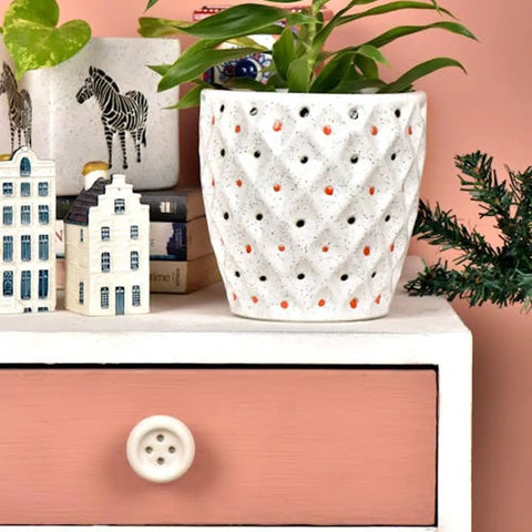 Decorative plant pot on a pink and white drawer with a button knob, surrounded by miniature house models and a zebra cup.