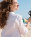 Person enjoying beach breeze with a black fan from Four Pack USB Rechargeable Mini Handheld Fans Set With 3 Speeds