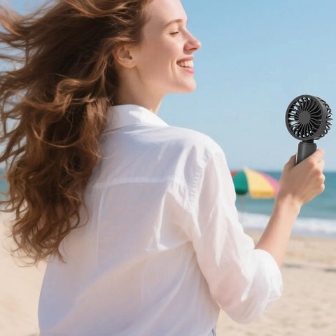 Person enjoying beach breeze with a black fan from Four Pack USB Rechargeable Mini Handheld Fans Set With 3 Speeds