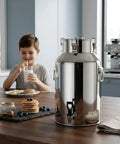Stainless Steel Milk Can With Airtight Lid Built To Last Heavy Duty Food Grade Tank for Milk Storage in a kitchen with child drinking milk.