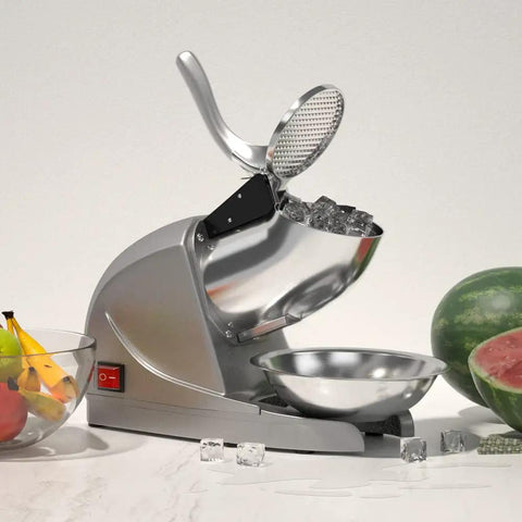 Electric Ice Shaver With Prevent Splash Design 3 Blade Snow Cone Machine 380W Shaved Ice Maker Cranks Out Up To 286 Lbs Per Hour Home Use Ice Crusher With Free Ice Pick Silver displayed on kitchen countertop with fruit and ice cubes.