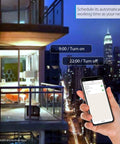 Hand holding smartphone controlling BR30 Smart LED Flood Bulbs 13W 1300 Lumens RGB from a balcony with city view at night.