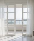 View through white sliding doors with sheer curtains revealing an outdoor balcony and ocean scene.