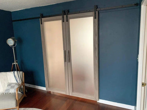 Kick Up Your Spaces With Top Shelf Double Sliding Barn Doors 42 X 96 Inches Featuring Ginger Ash Finish Frosted Glass Inserts Include Rugged Matte Black Rail Track And Complete Hardware Kit For Fast Bedroom Remodels, installed in a blue wall.