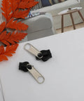 12 Pack Black Zipper Repair Kit Universal Sliders Replacement Zip Pullers for Clothes Bags Luggage and More, two black sliders close-up on table