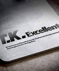 Close-up of T.K. Excellent logo on a metallic surface with engraved text about fastening materials.