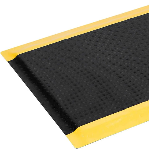 Anti Fatigue Standing Mat For Workshops 3 By 5 Feet Beefed Up Industrial Grade Ergonomic Floor Mat Nearly One Inch Thick With Non Slip Surface And Yellow Border For Leg And Back Pain Relief On Long Shifts, featuring a close-up view of the mat's black non-slip surface and yellow edges.