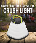 Crush Light Solar Powered Camping Lantern With Collapsible Design on wooden surface, outdoors with car and trees in background.