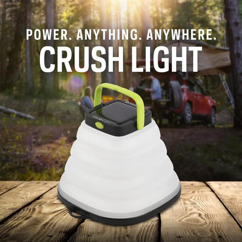 Crush Light Solar Powered Camping Lantern With Collapsible Design on wooden surface, outdoors with car and trees in background.