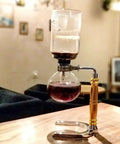 Straight Fire Borosilicate Glass Siphon Coffee Maker With Heavy Duty Stainless Base And Precision Alcohol Burner For Smooth Cold Brew And Iced Coffee Vibes Tabletop Ready on wooden surface.
