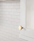 Slick Modern Cabinet Knobs With A Fresh Champagne Bronze Finish on a white cabinet against tiled wall.