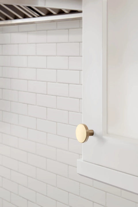 Slick Modern Cabinet Knobs With A Fresh Champagne Bronze Finish on a white cabinet against tiled wall.