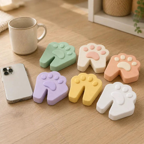 Six Pack Soft Foam Paw Shaped Door Stoppers For Finger Pinch Protection In Pastel Colors Sage Cream Peach Lavender Butter Yellow White on table.