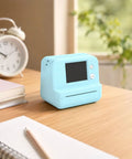 Rock This Slick AI Voice Mini Thermal Printer With Bright Display And Awesome Creative App For Kids Speech To Line Art Drawing Anime Sketch And Hype Storytelling Portable Prints on a desk with notebooks.