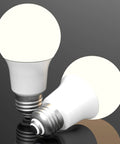 Two Three Way A19 LED Light Bulbs, 40 60 100 Watt Equivalents, E26 Socket, glowing on a reflective surface