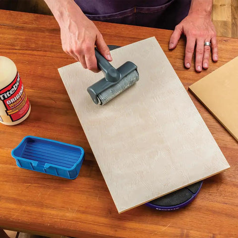 Using the Go-To 5 Inch Wood Glue Roller with thermoplastic rubber roller on a wooden board with silicone rest on table