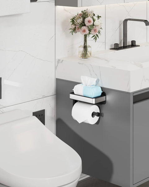 Toilet Paper Holder With Top Shelf And Phone Storage Adhesive And Screw Wall Mount Matte Black Bathroom Organizer For Washroom And RV Space Saving 7 Point 1 Inch Wide installed next to a sink with flowers.