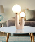 Double-Headed Nordic Modern Table Lamp With Plant Art on round table in living room, beside gray sofa, warm glow, plug in with switch