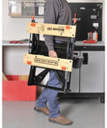 Person carrying a Portable Work Bench With Vise And Adjustable Height Legs, Heavy Duty Steel Frame Supports Up To 450 Lbs, ideal for projects.