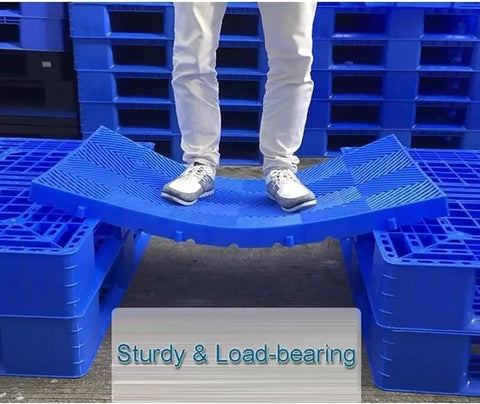 Person standing on interlocking plastic pallet with ventilated grid for garage storage and warehouse use, waterproof durable 60x60x3cm blue