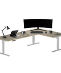 Game Changer Electric Lift L Shaped Standing Desk 88 Inch Wide Corner Office Table with dual monitors and accessories.