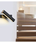 Elevate Your Home Vibe With This Sleek Black Metal Swivel Wall Sconce Led Lighting For Bedroom Living Room And Hallways Rustproof Adjustable Accent Lamp mounted on a white wall above wooden stairs.