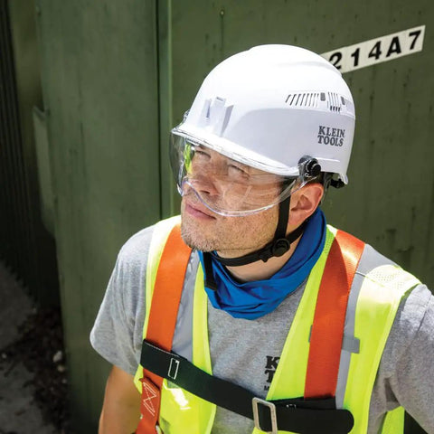 Worker wearing Klein Tools helmet with chin strap and safety vest outdoors
