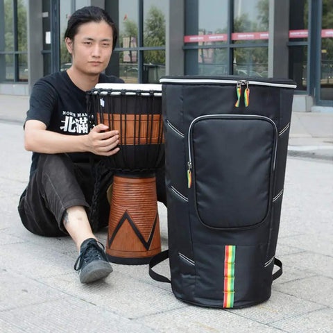 Rock Solid Protection For Your Everyday Jam, Hassle Free Djembe Gig Bag Built From Heavy Duty Oxford Fabric, Adjustable Double Straps, Water Repellent Shock Proof Case For 12 Inch African Drum, shown with a djembe.