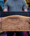 Person holding wooden cutting board with black finish, highlighting Cutting Board Oil And Wood Butcher Block Oil 128 Oz One Gallon Jug Brewed In USA.