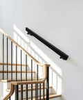 Badass Black Stainless Steel Wall Mount Handrail For Stairs And Hallways With Heavy Duty Support mounted on a wall beside stairs.