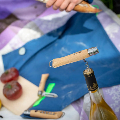 Nomad Camping Kitchen Utensil Kit with corkscrew knife on wine bottle, tomatoes on cutting board, outdoor scene.