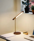 LED Wood Grain Desk Lamp With Wireless Charger And USB Port For Home Office on a desk next to a laptop and plants.