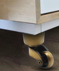 Four Piece Antique Brass Furniture Casters Crafted From Solid Cast Zinc Alloy featuring smooth 360 degree swivel rollers under a cabinet.